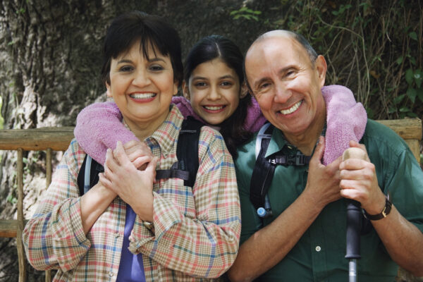 A family of three smiles into the camera. The mom is on the left and the father is on the right. The daughter poses between them.