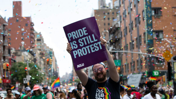 An individual holds a sign that says "Pride Is Still Protest" in the middle of a crowded pride parade