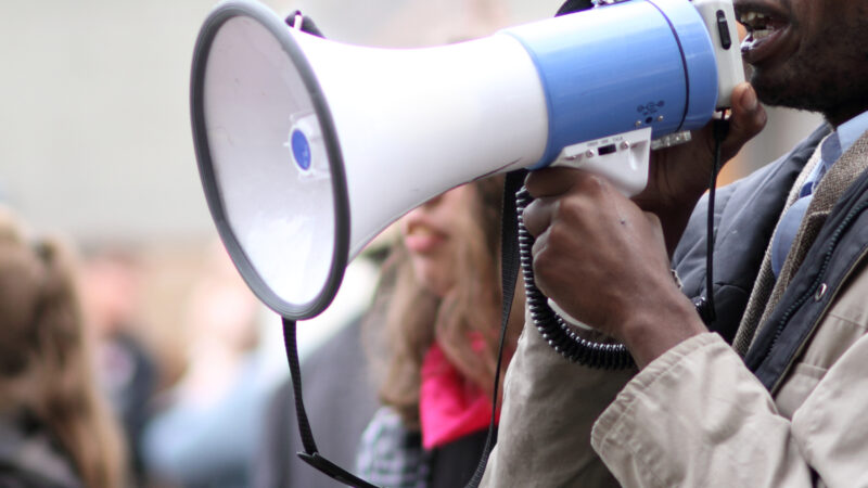 A black male protestor speaks into a megaphone