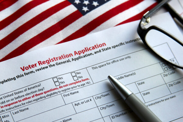 A voter registration application, a pen, an American flag, and a pair of glasses