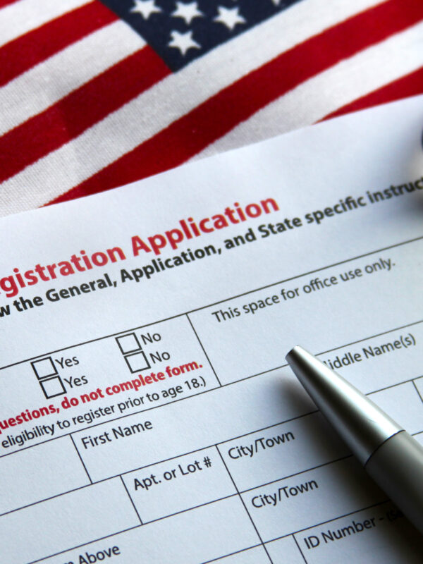 A voter registration application, a pen, an American flag, and a pair of glasses