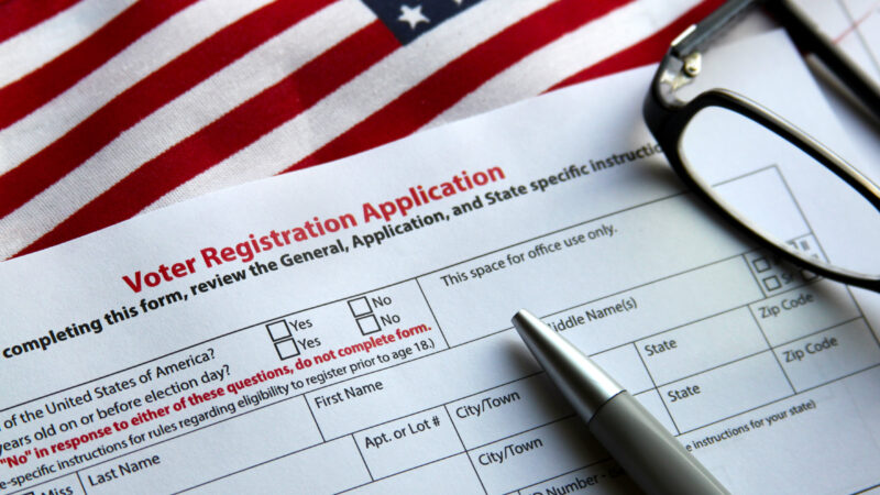 A voter registration application, a pen, an American flag, and a pair of glasses