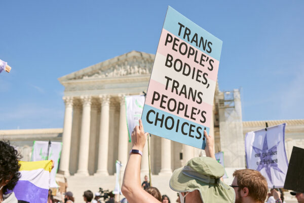 Person holding a sign in front the Supreme Court that reads Trans People's Bodies, Trans People's Choices