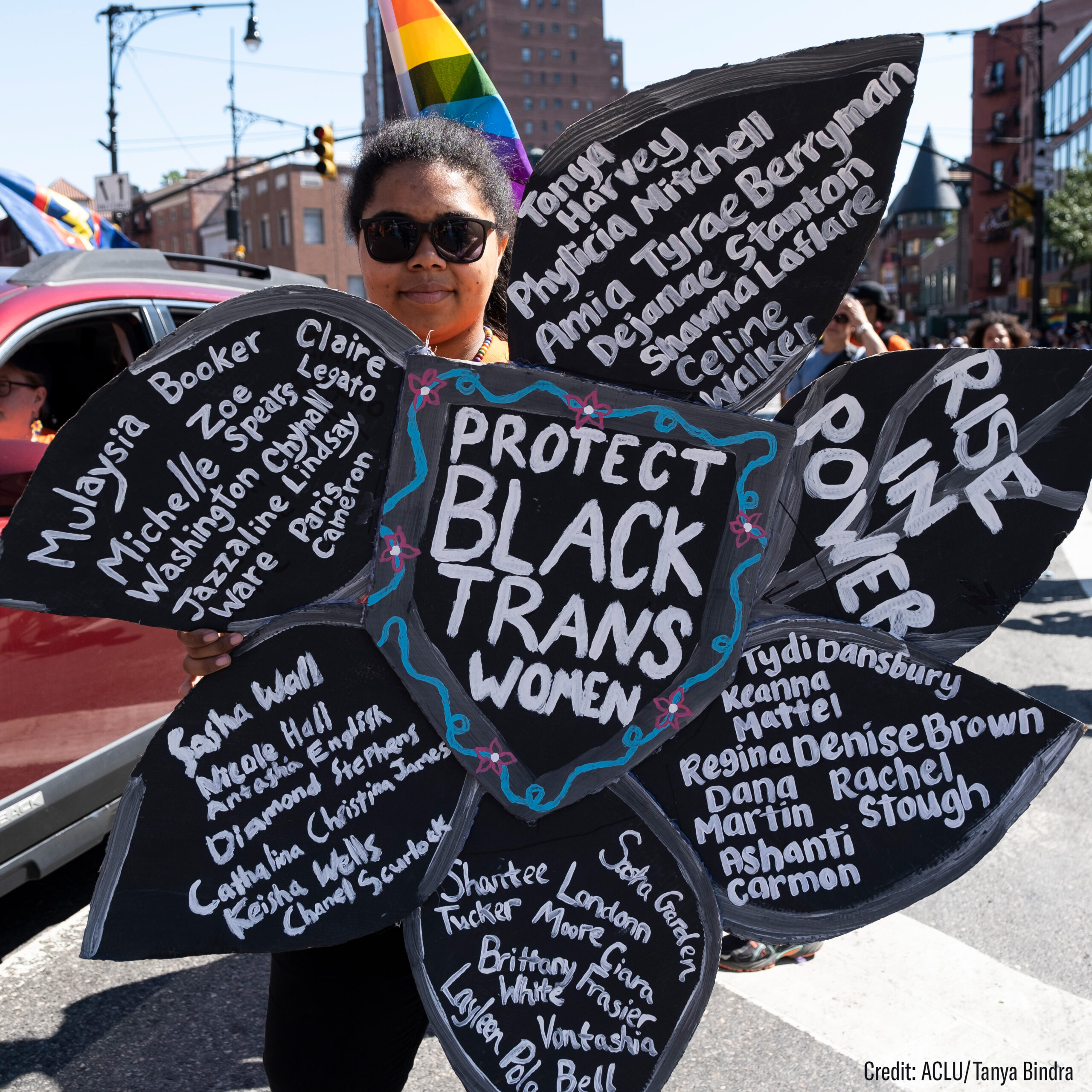 Woman holding flower-shaped sign with phrases supporting Black Trans women