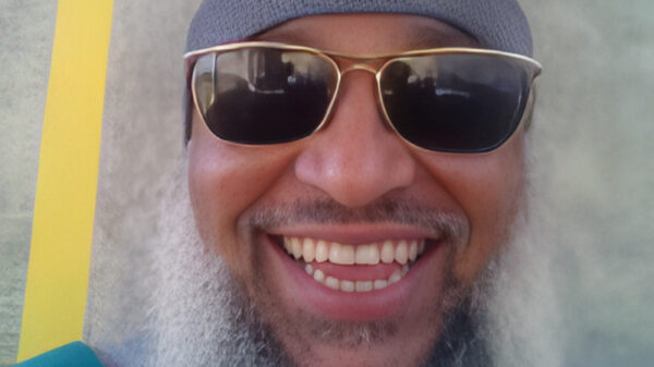 Headshot of man with a long beard in sunglasses and a hat.