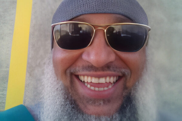 Headshot of man with a long beard in sunglasses and a hat.