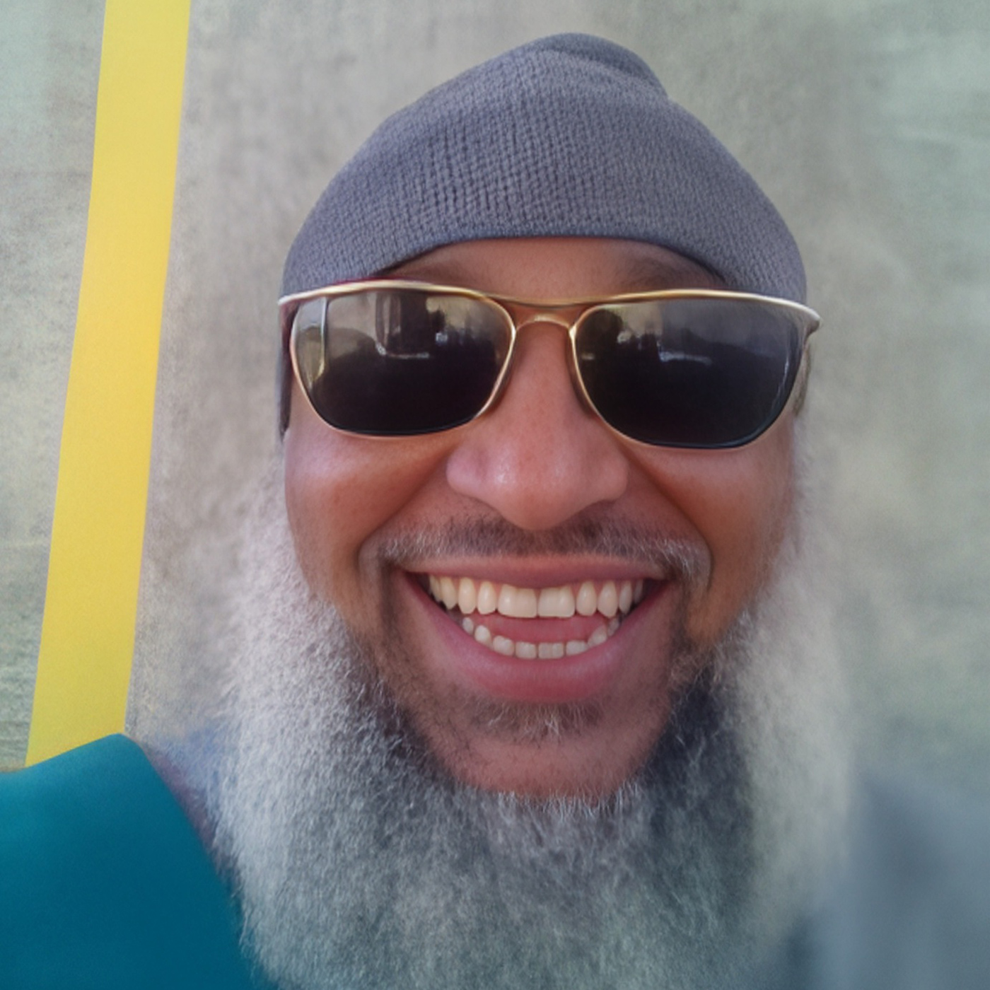 Headshot of man with a long beard in sunglasses and a hat.