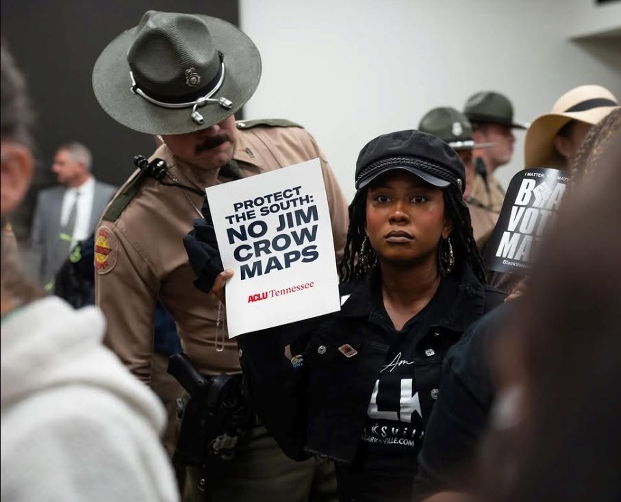White officer stares at a Black woman holding a sign that says No Jim Crow Maps.