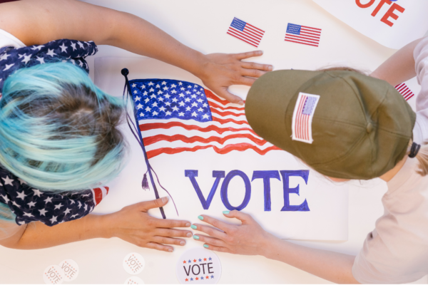Image of a two hands reaching across the table with a patriotic sign that says VOTE in the middle.