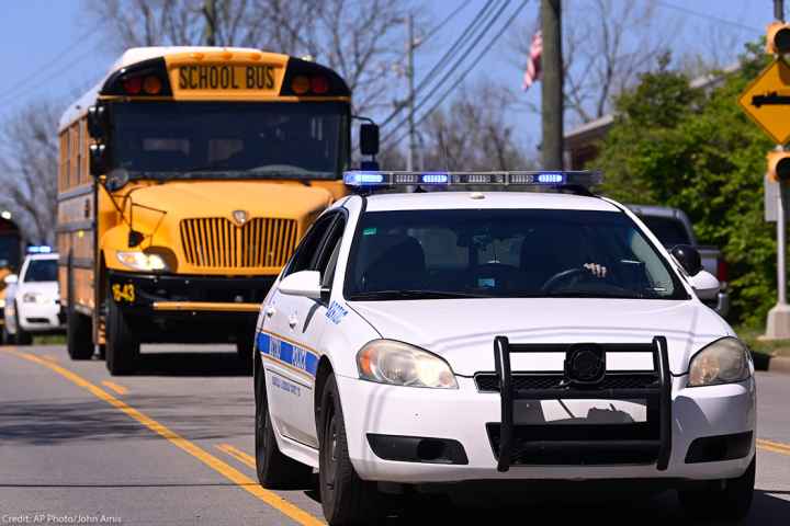 A police car driving on a road in front of a school bus.