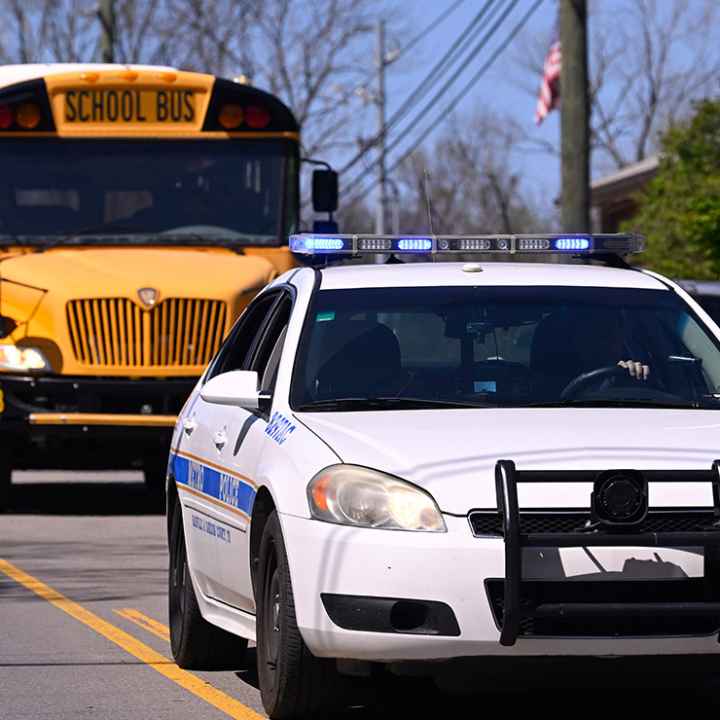 A police car driving on a road in front of a school bus.